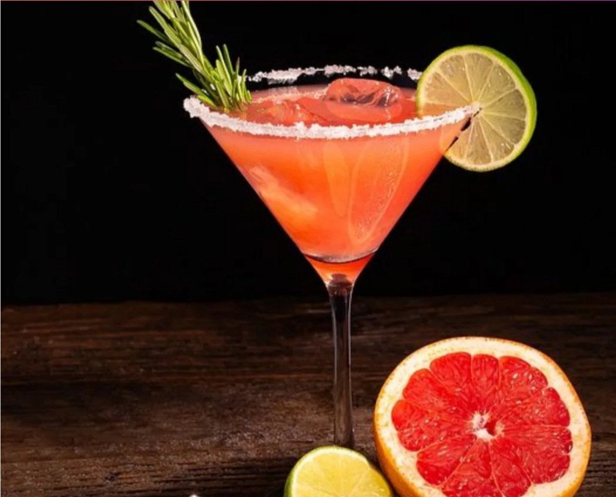 Coctel rosado en copa martini escarchada con romero, lima y toronja sobre madera