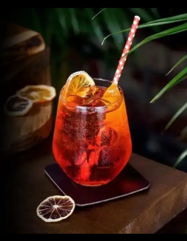 Coctel rojo con hielo y rodaja de naranja servido en vaso con pitillo